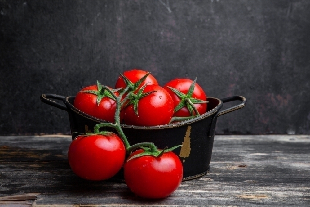 A bunch of tomatoes rich in MSM in a pot on a old wooden and black background. side view