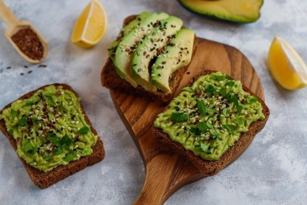 Avocado open toast with avocado slices lemon flax seeds sesame seeds black bread slices top view