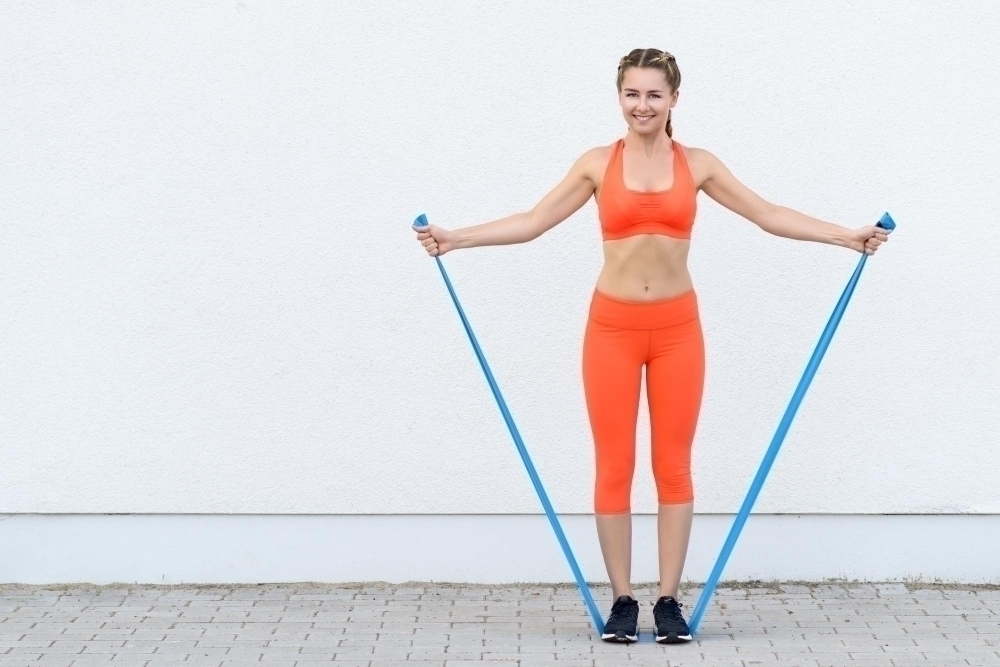 Full length portrait of young woman exercising with resistance band against wall